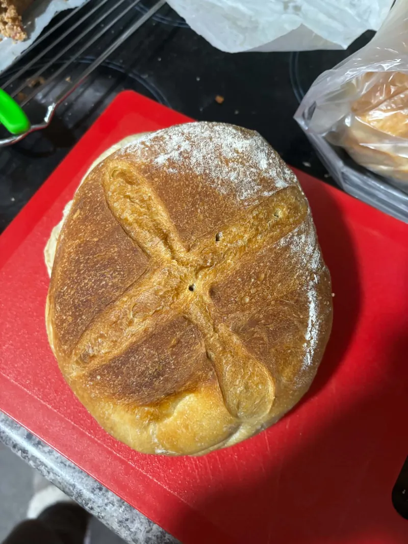 Round sourdough loaf with a cross score and light flour dusting on a red board