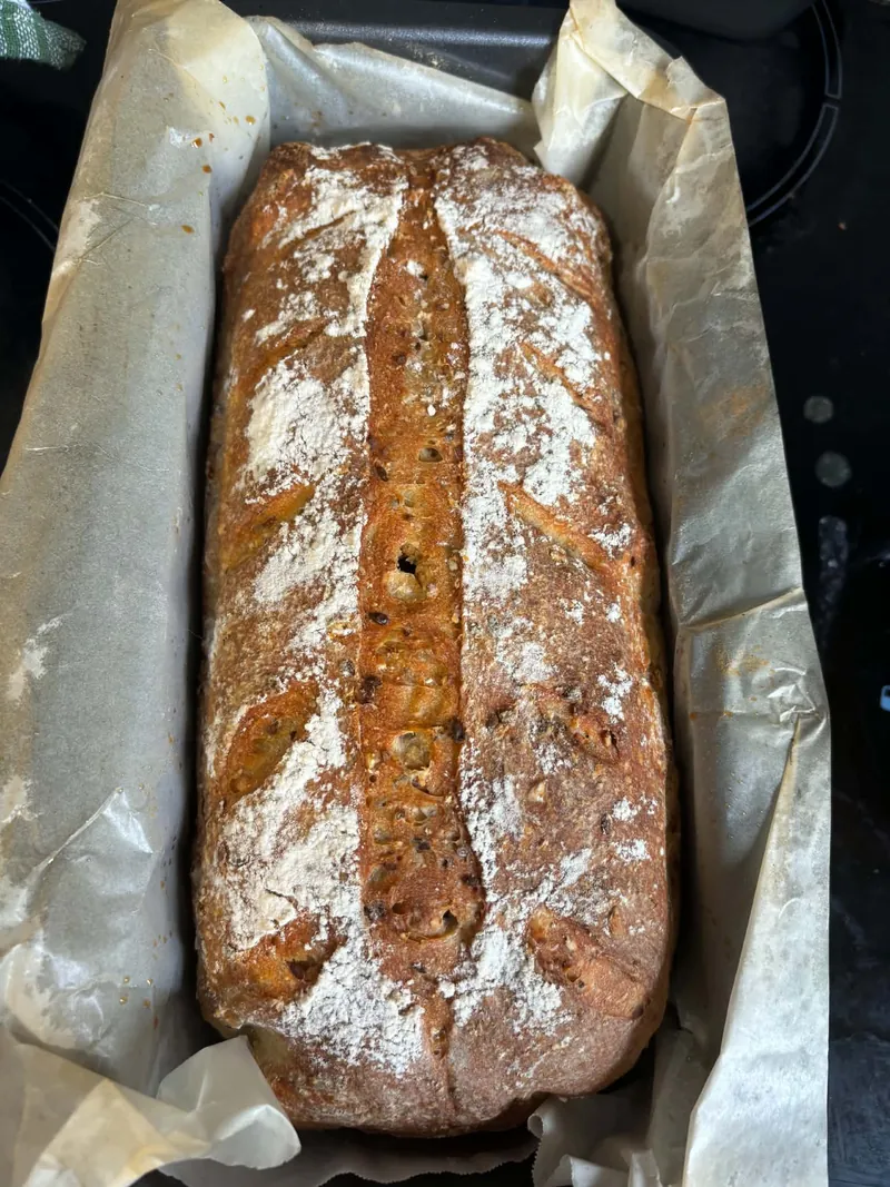 Long seeded sourdough loaf in a parchment-lined loaf pan, from above