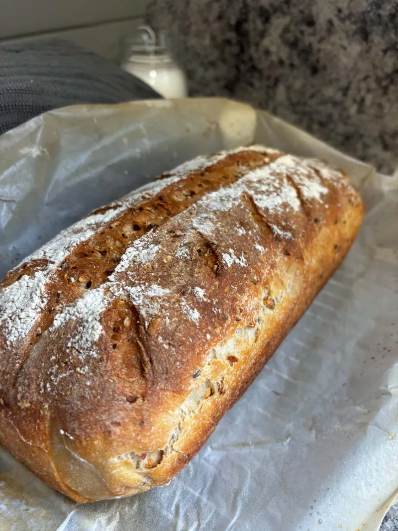 Seeded, flour-dusted sourdough batard on baking paper